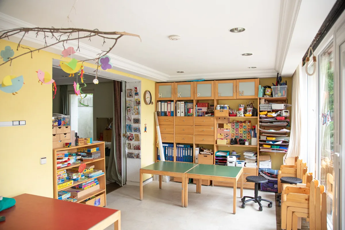Heller Bastelraum der Kita Kinderwerkstatt mit Holzregalen, Spielen und Tischen, darüber selbstgebastelte Papiervögel am Ast