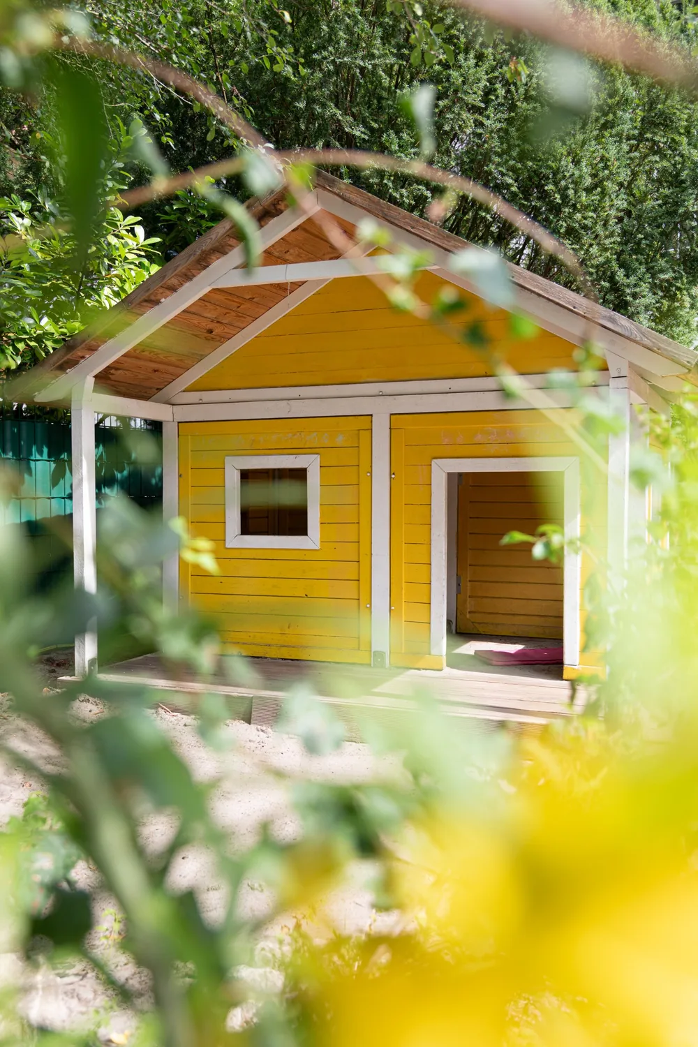 Gelbes Holzspielhaus mit weißen Fensterrahmen im Garten der Kita Kinderwerkstatt Münster