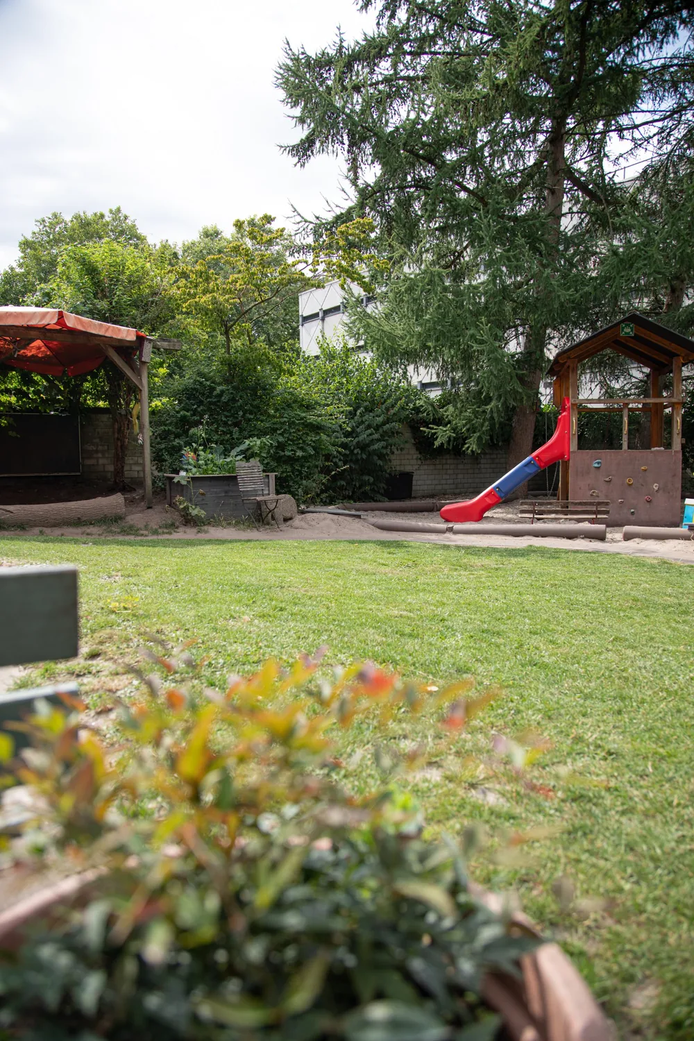 Garten der Kita Kinderwerkstatt mit Rasenfläche, Spielplatz mit Rutsche und Hochbeet