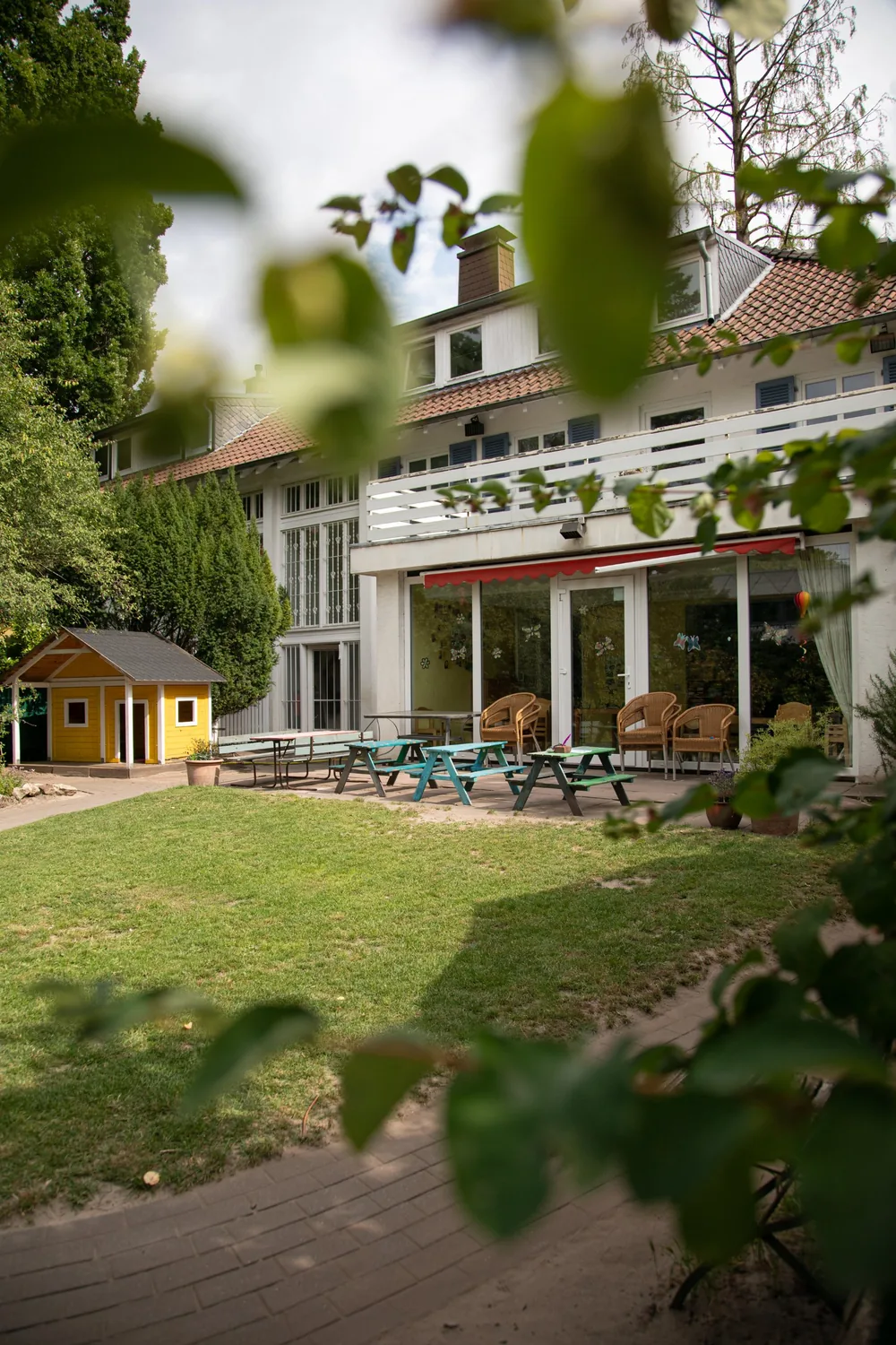 Gartenseite des Kita-Gebäudes mit Terrasse, bunten Picknickbänken und gelbem Spielhaus