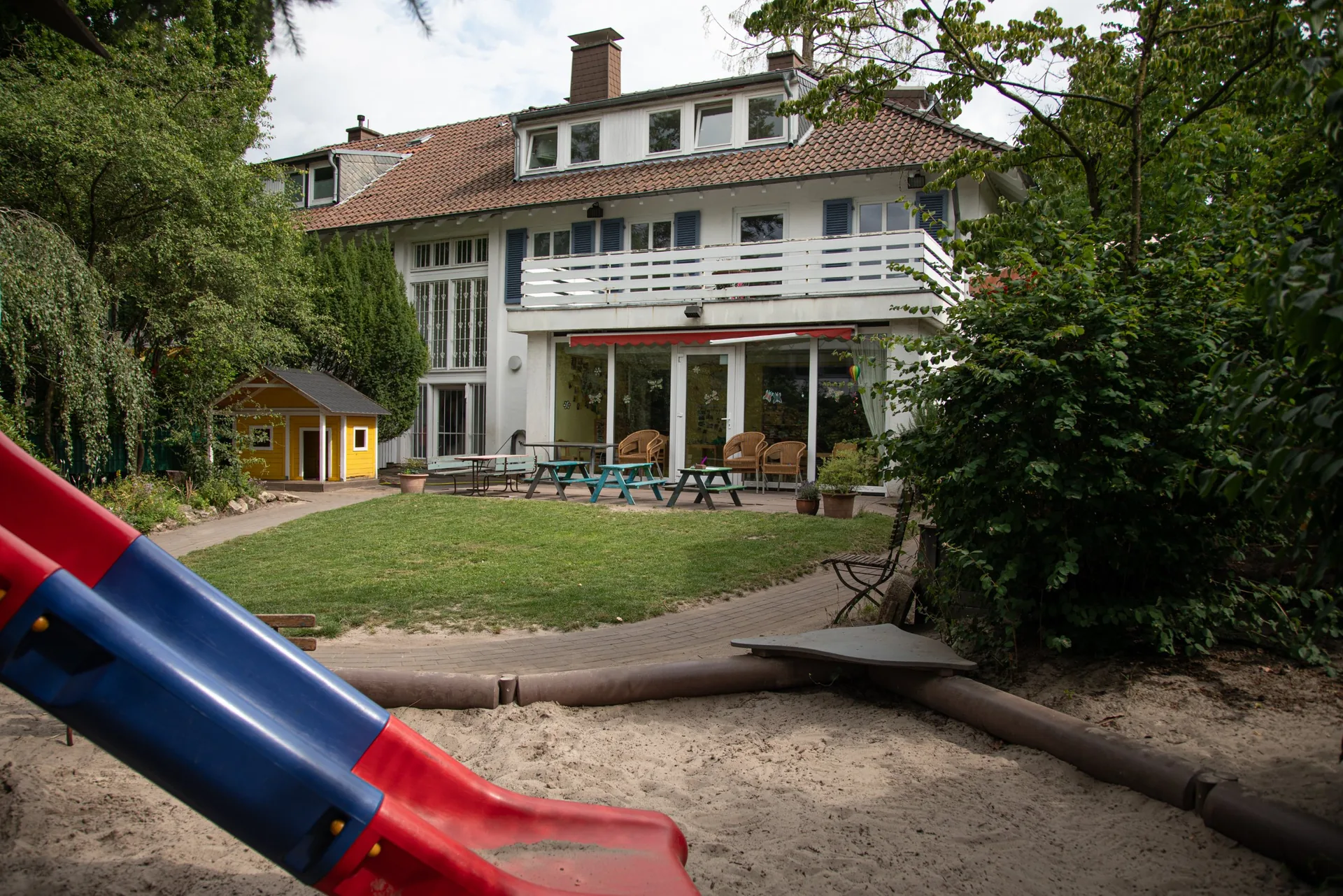 Garten und Gebäude der Kita Kinderwerkstatt Münster mit Terrasse, Spielhaus und Rutsche im Vordergrund