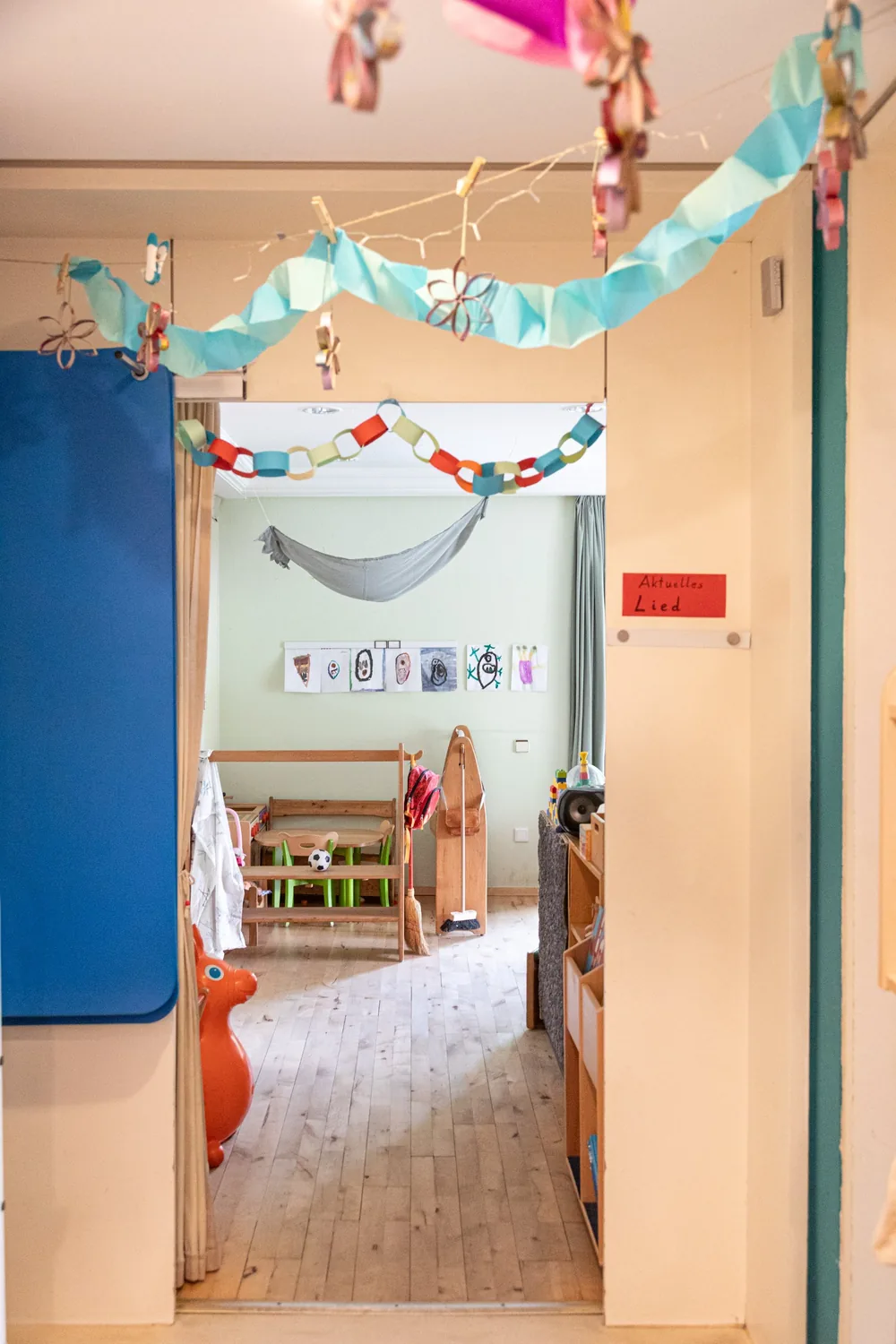 Blick durch einen Durchgang in einen Gruppenraum mit Hängematte, Kinderzeichnungen und Papiergirlanden